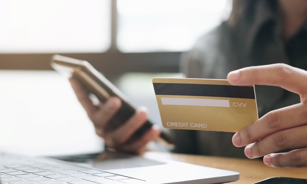 Person holding a credit card while using a smartphone and laptop