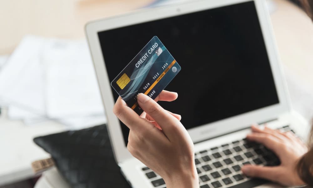 Person holding a credit card while using a laptop